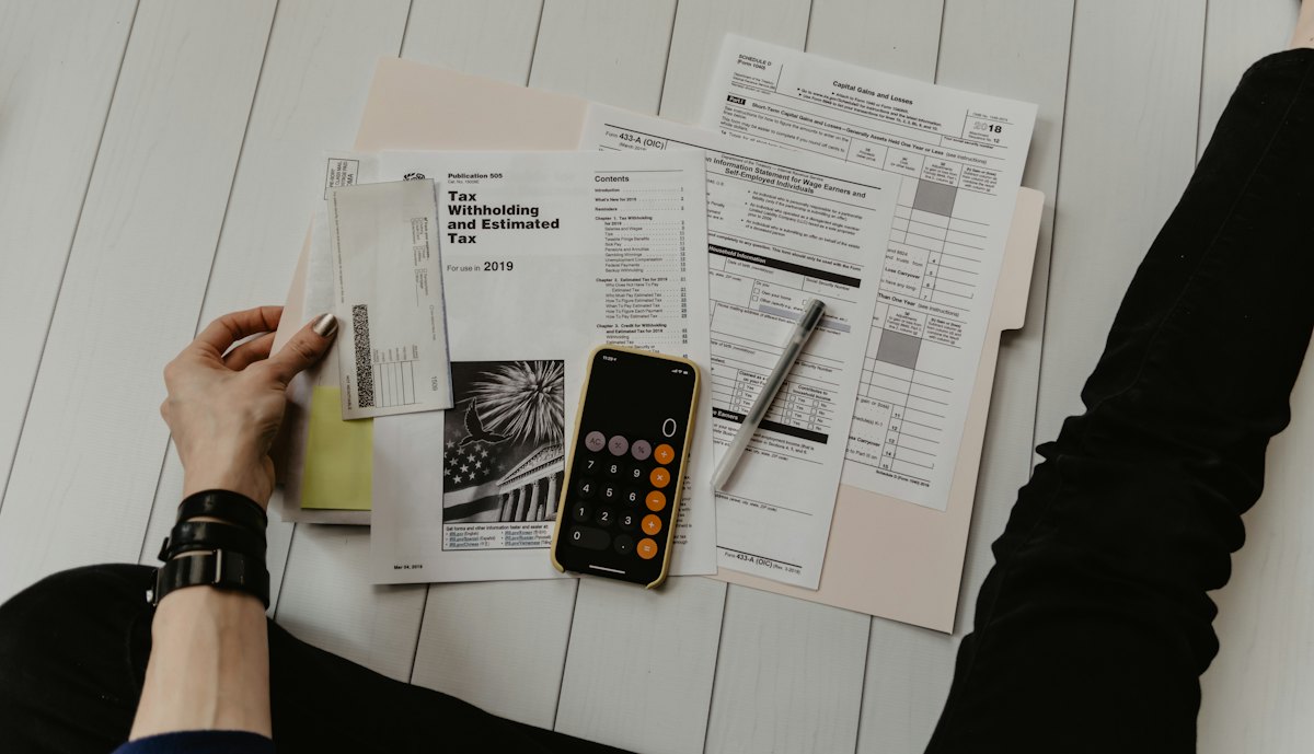 Paper financial forms spread out with a calculator and a pen.